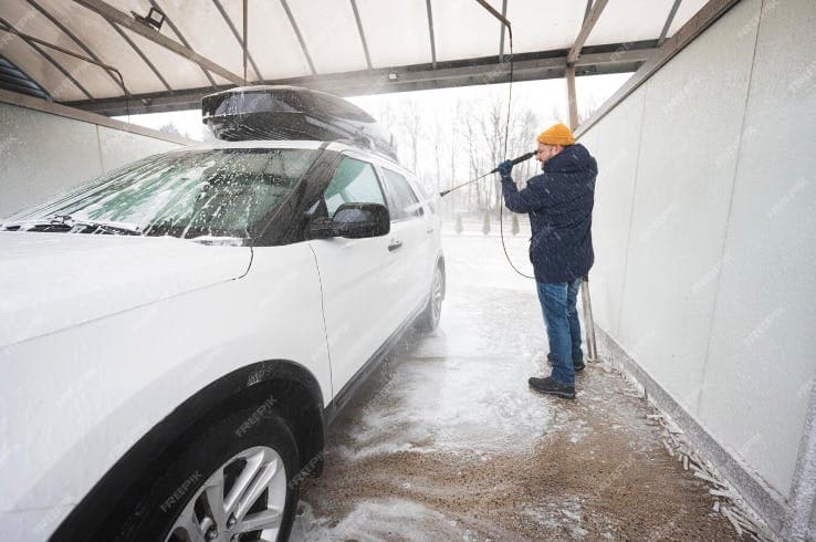 Adult male power washing the side of a SUV with a rooftop box on it.